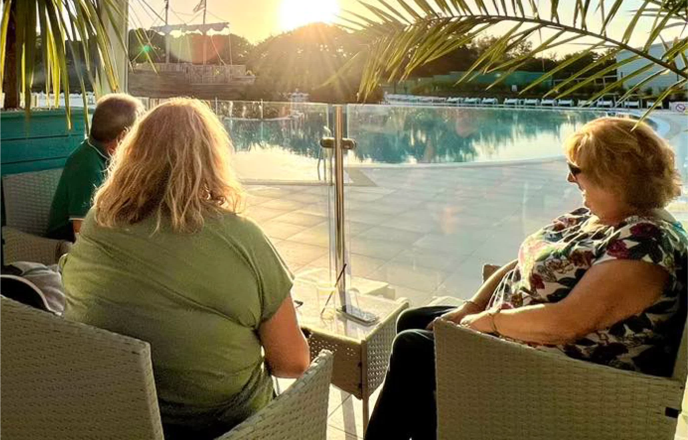 Three people relax by a serene pool at sunset, framed by palm leaves. the warm sunlight glows on their faces as they enjoy the peaceful outdoor setting.