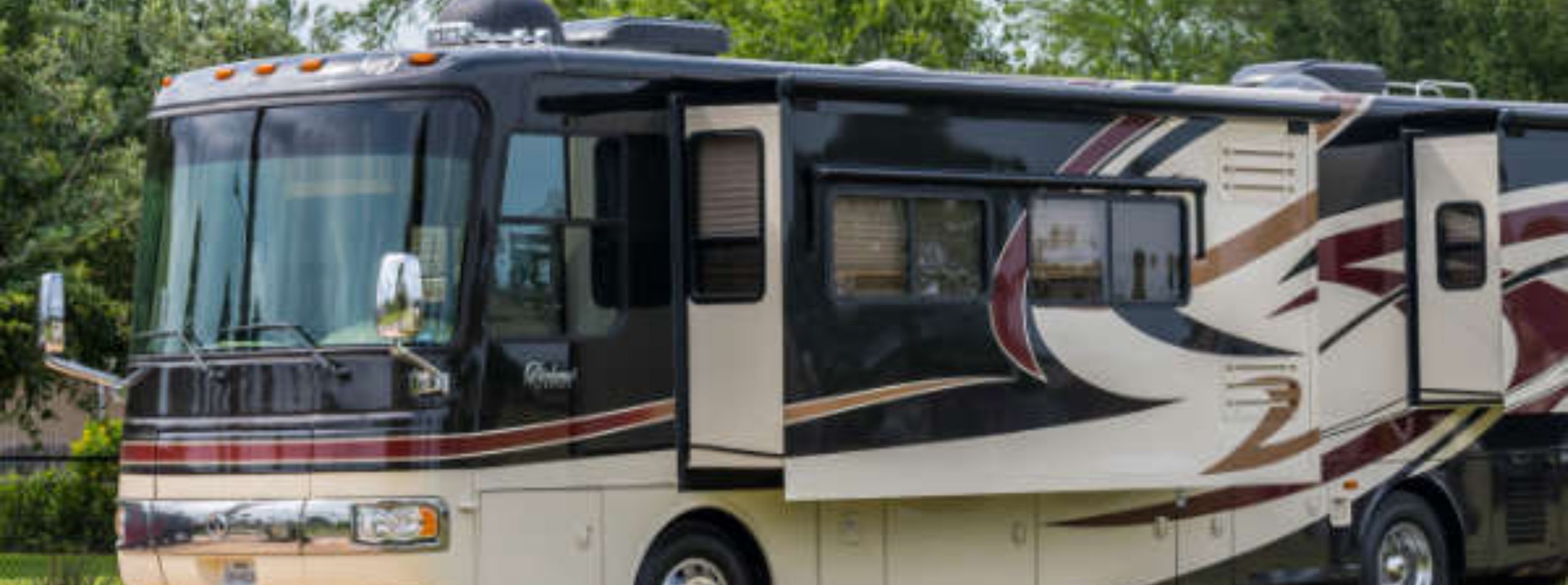 Side view of a large, modern RV parked outdoors at a luxury campsite, featuring a brown and cream color scheme with decorative swirls.