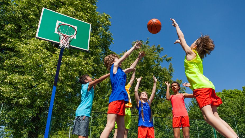 children playing basketball on the outdoor court at Monkey Tree Holiday Park under clear blue skies