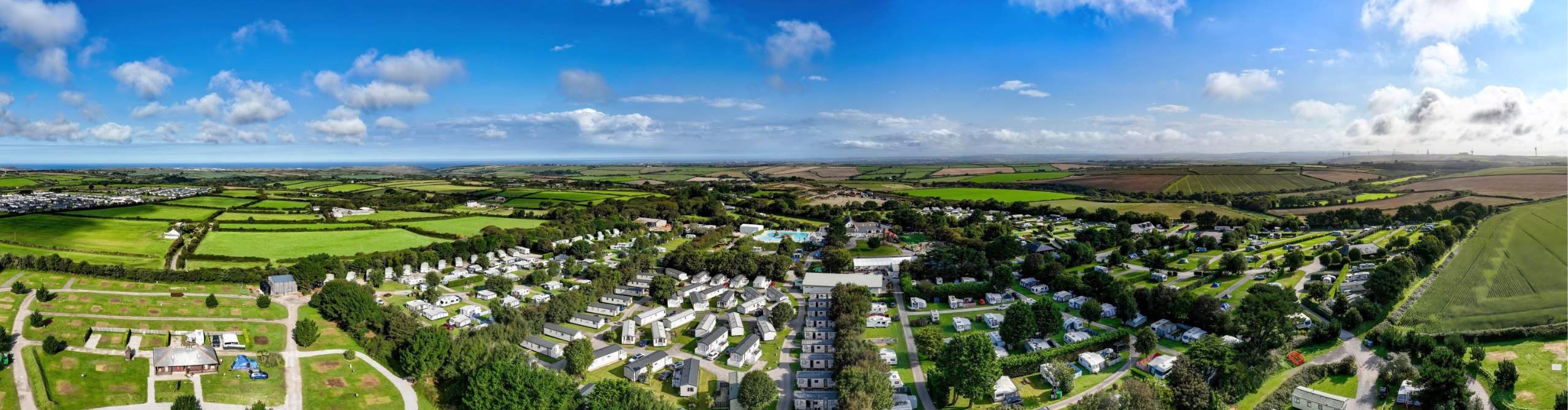 Panoramic aerial view of a rural landscape featuring clusters of holiday homes, extensive green fields, and a clear sky.