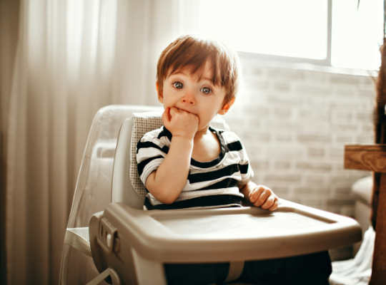 A child in a highchair with his hand in his mouth