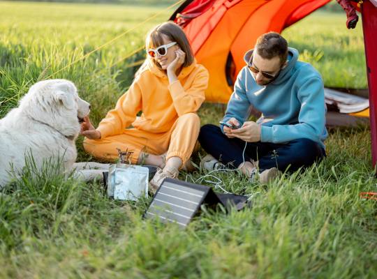 A couple outside their tent with the gentleman holding a mobile phone and the lady smiling at her dog